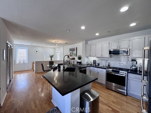 33423 Winston Way, Unit C Temecula, CA 92592 - Photo 15 of 39 a kitchen with stainless steel appliances granite countertop a stove a refrigerator a sink a dining table and chairs with wooden floor