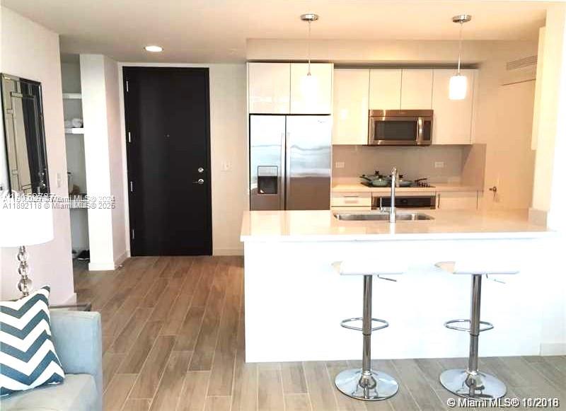 999 Southwest 1st Avenue, Unit 2115 Miami, FL 33130 - Photo 11 of 27 a kitchen with stainless steel appliances kitchen island granite countertop a refrigerator a stove and a sink with wooden floor