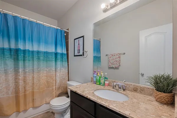 a bathroom with a granite countertop sink a toilet a mirror and shower curtain