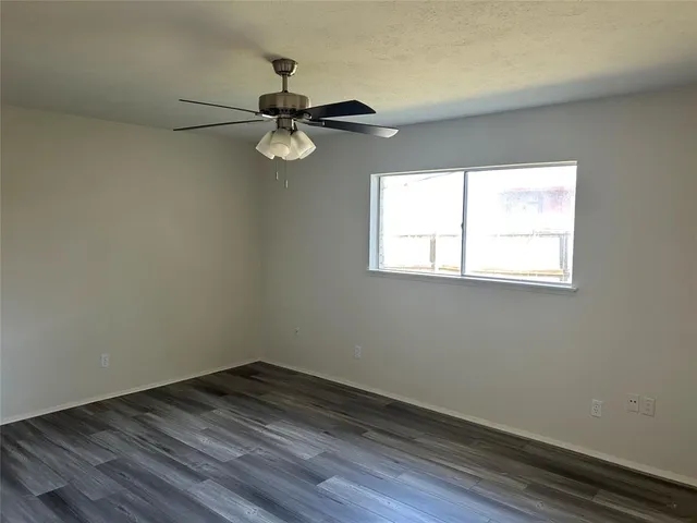 an empty room with wooden floor fan and windows