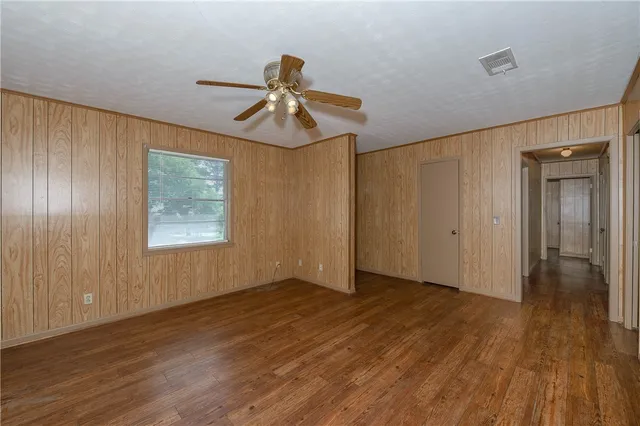 an empty room with wooden floor chandelier fan and windows
