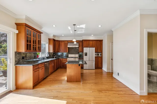 a kitchen with stainless steel appliances granite countertop a refrigerator a sink dishwasher a oven and a dining table with wooden floor