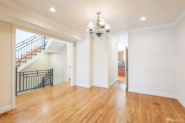 a view of an empty room with wooden floor and a chandelier