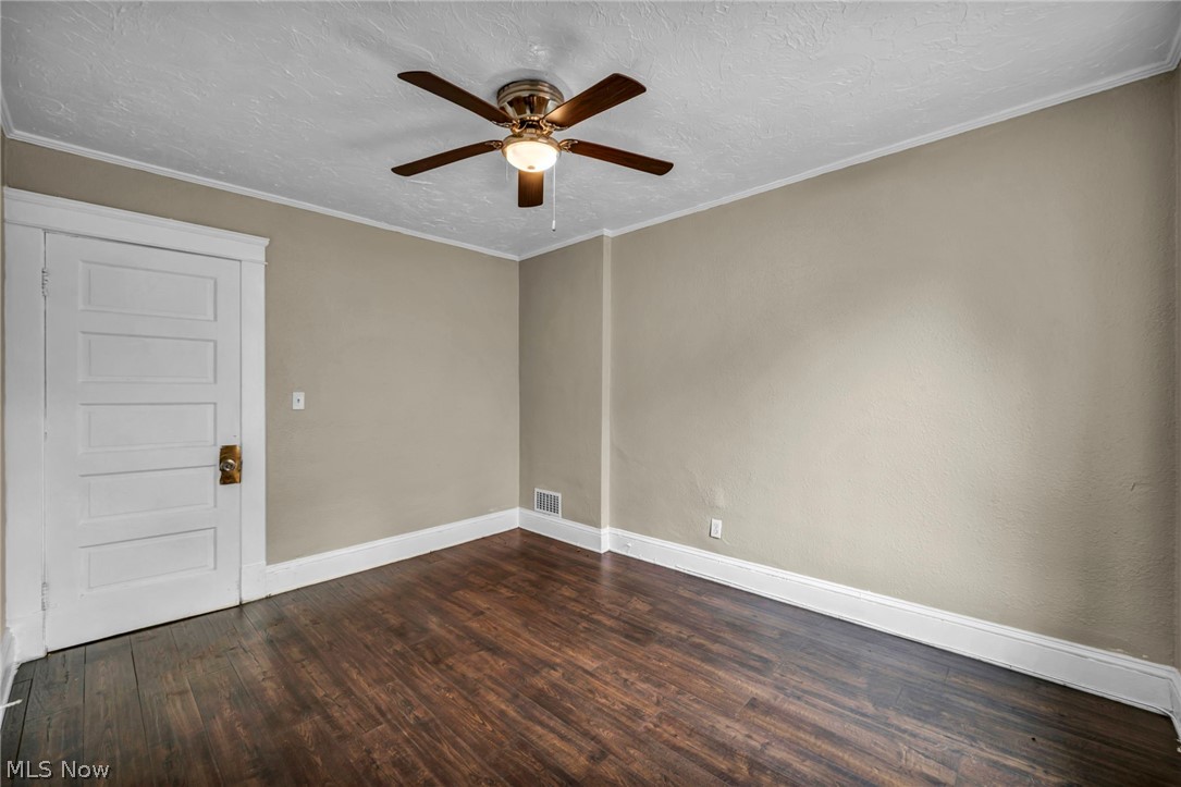 1677 Carlyon Road East Cleveland, OH 44112 - Photo 26 of 41 Unfurnished room featuring a textured ceiling, ornamental molding, dark wood-style flooring, and ceiling fan