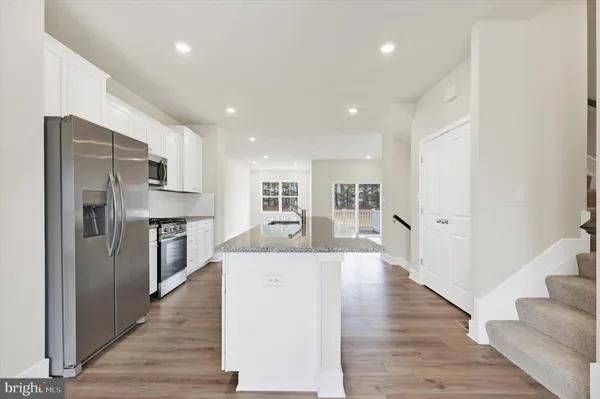 a large kitchen with stainless steel appliances kitchen island a stove a refrigerator a oven and a sink with wooden floor