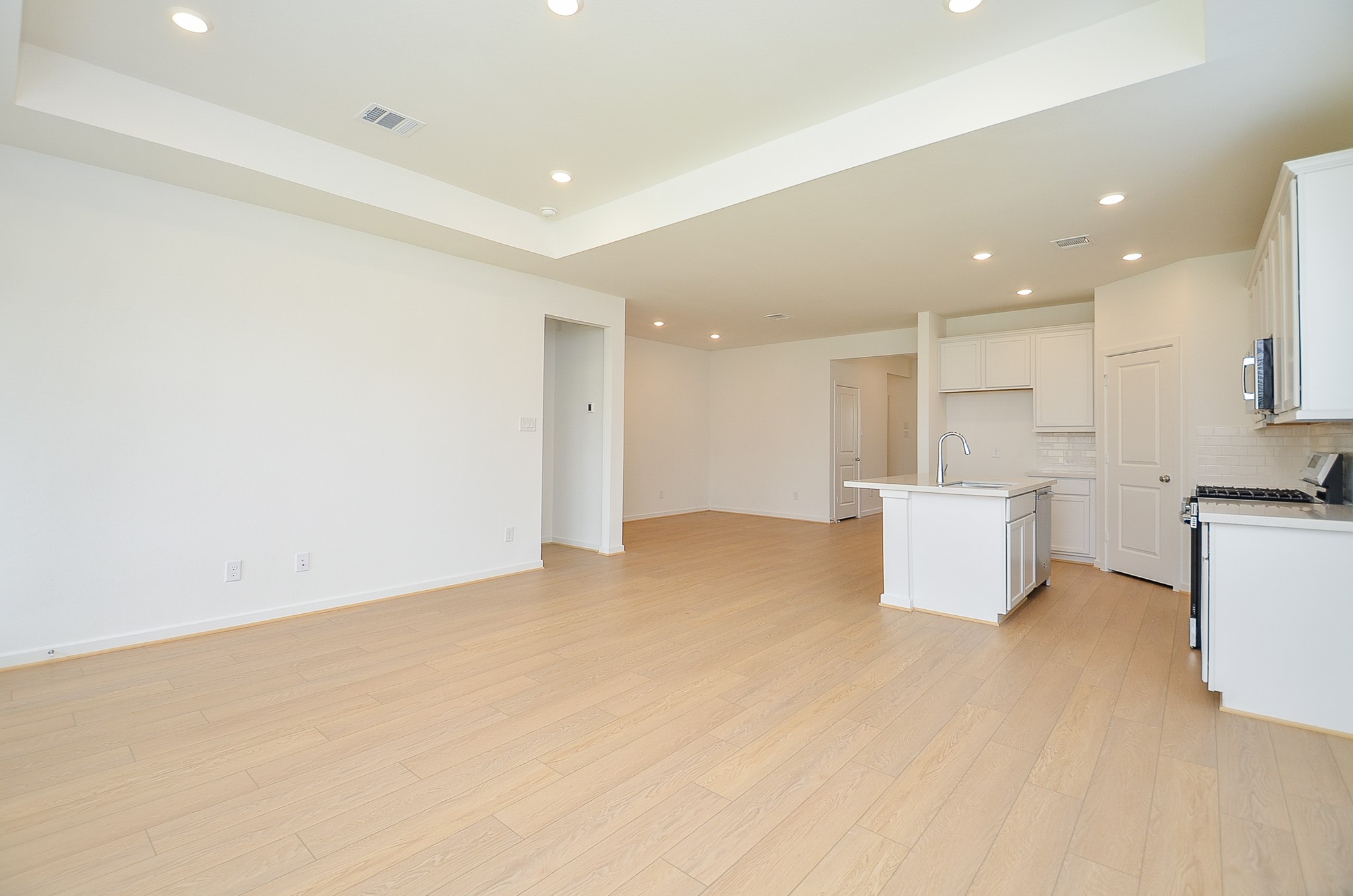 9727 Rialto Hts Drive Cypress, TX 77433 - Photo 18 of 37 This photo features a bright, open-concept kitchen and living area with large windows and recessed lighting. The kitchen includes modern appliances, a central island with a sink, and white cabinetry, creating a clean, airy feel.