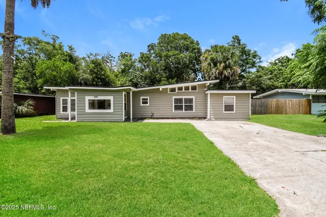 a backyard of a house with plants and large tree