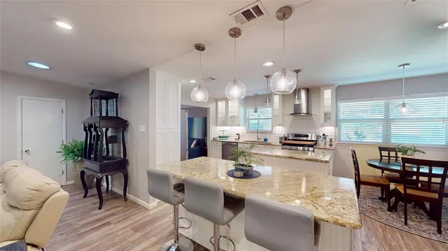 a kitchen with stainless steel appliances kitchen island granite countertop a refrigerator a stove a dining table and chairs with wooden floor