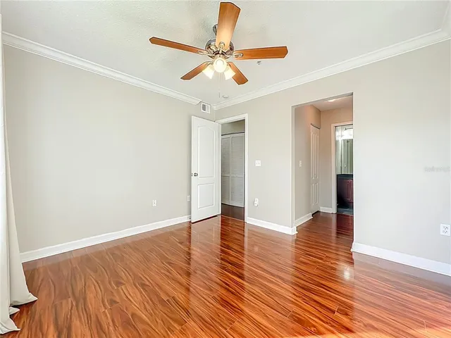a view of an empty room with wooden floor and a ceiling fan