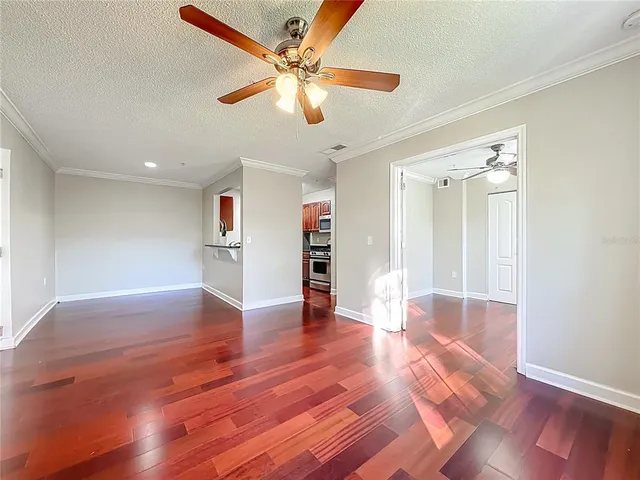a view of an empty room with wooden floor and a ceiling fan