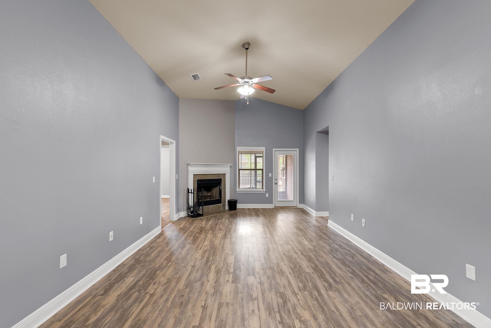 22076 Garland Loop Silverhill, AL 36576 - Photo 3 of 27 Spacious living area featuring vaulted ceilings, wood-finish flooring, a fireplace with a white mantel, a ceiling fan, and a glass-paneled door to the exterior
