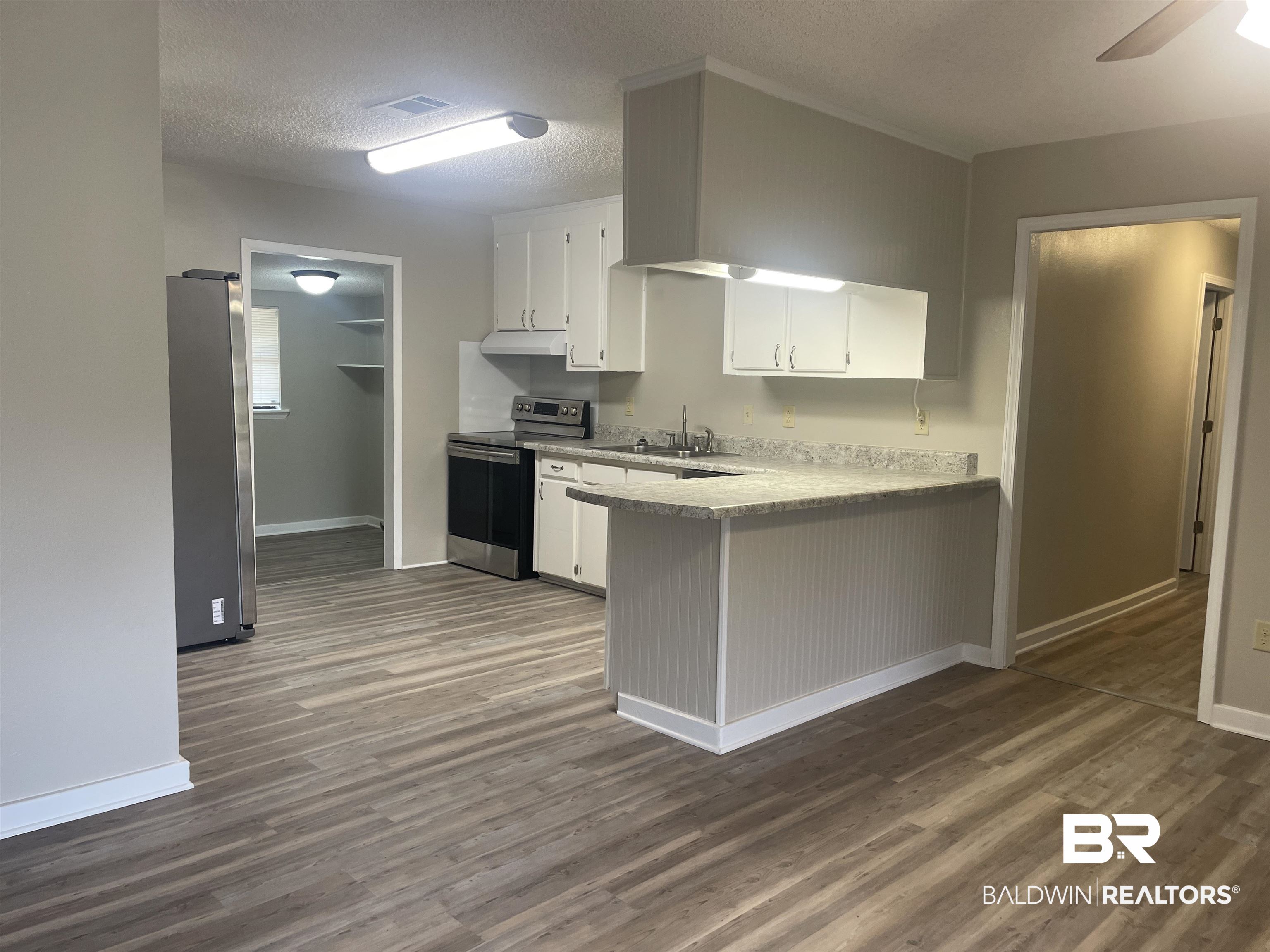 28414 Highway 31 Flomaton, AL 36441 - Photo 4 of 11 Kitchen with under cabinet range hood, New LVP Flooring, white cabinets, and stainless steel appliances