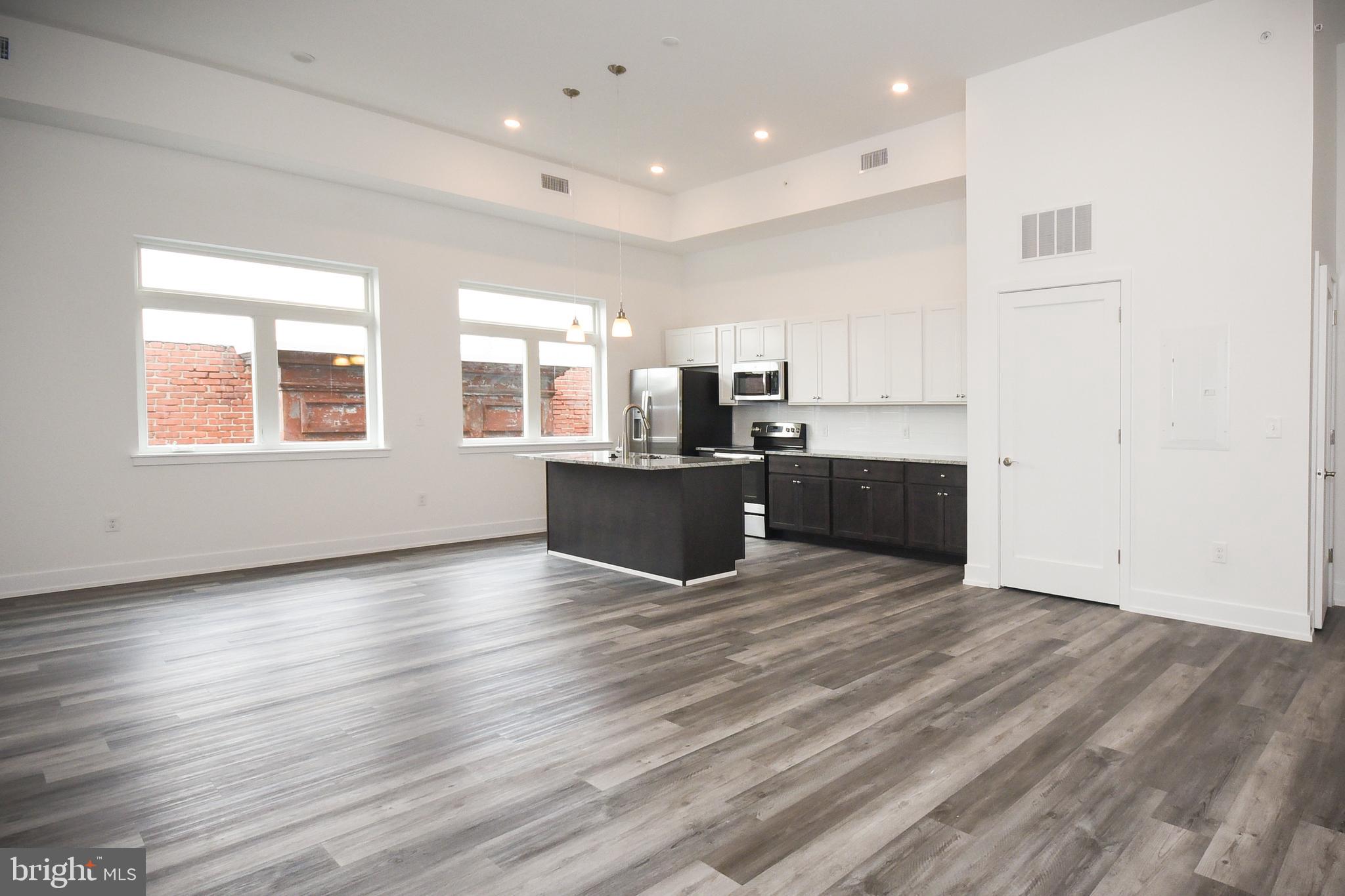 6164-66 Ridge Avenue, Unit 302 Philadelphia, PA 19128 - Photo 8 of 15 an empty room with kitchen view and wooden floor