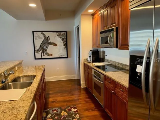 a kitchen with stainless steel appliances granite countertop a refrigerator a stove and a sink with wooden floor