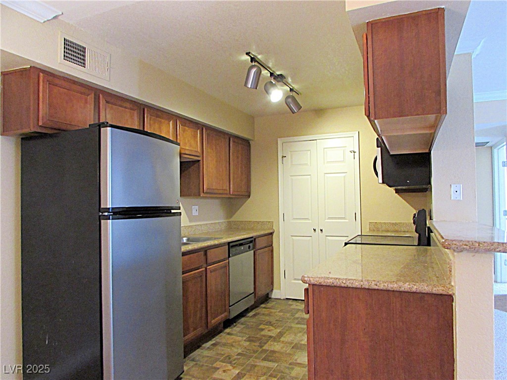 3135 South Mojave Road, Unit 260 Las Vegas, NV 89121 - Photo 6 of 23 Kitchen with appliances with stainless steel finishes, track lighting, brown cabinetry, stone finish floors, and light stone counters