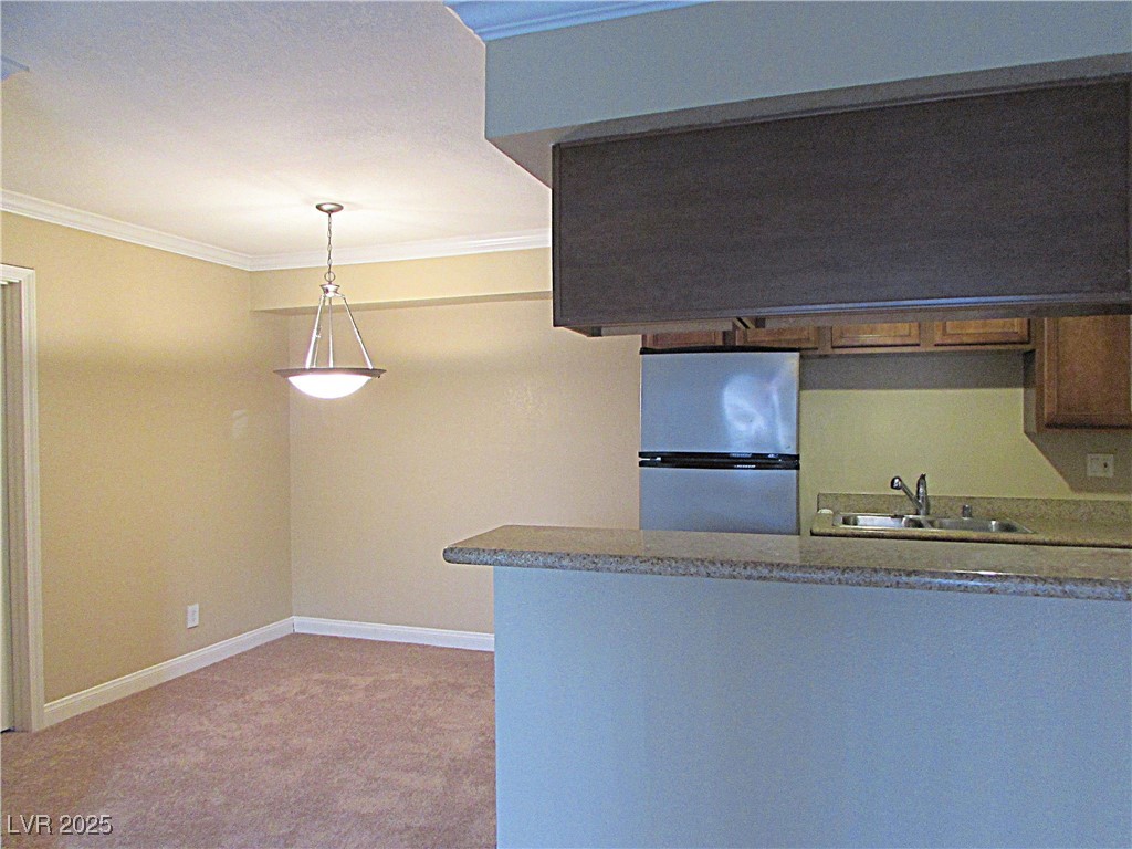 3135 South Mojave Road, Unit 260 Las Vegas, NV 89121 - Photo 7 of 23 Kitchen with ornamental molding, freestanding refrigerator, light carpet, hanging light fixtures, and a peninsula