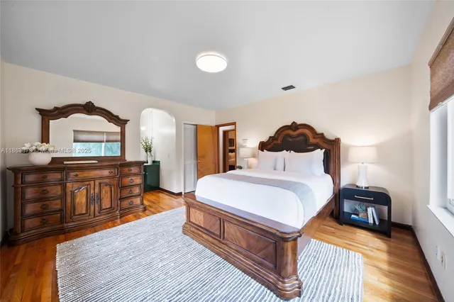 a spacious bedroom with a bed a dresser and wooden floor