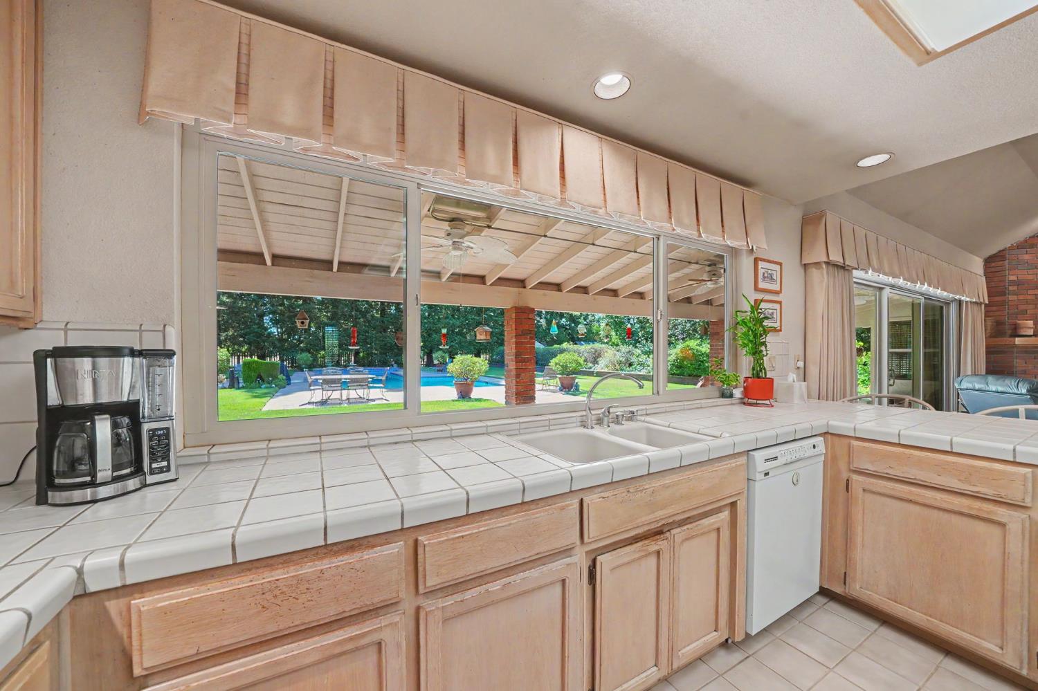 9069 Bader Road Elk Grove, CA 95624 - Photo 15 of 70 Kitchen with a tile countertop, double basin sink, wood-finish cabinetry, and picture window to backyard patio & pool