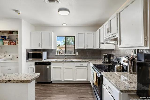 a kitchen with white cabinets appliances a sink and a window