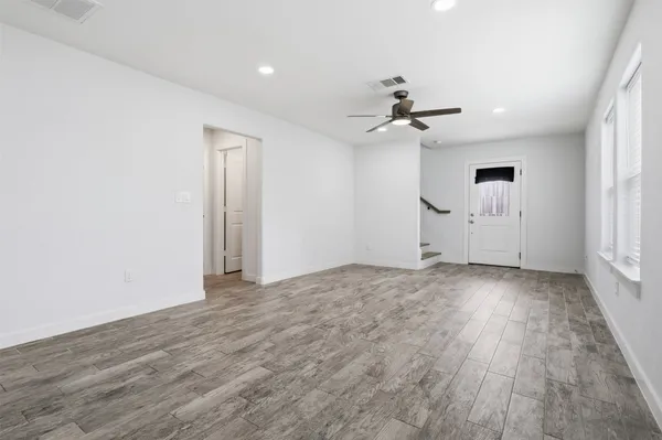 an empty room with wooden floor ceiling fan and windows
