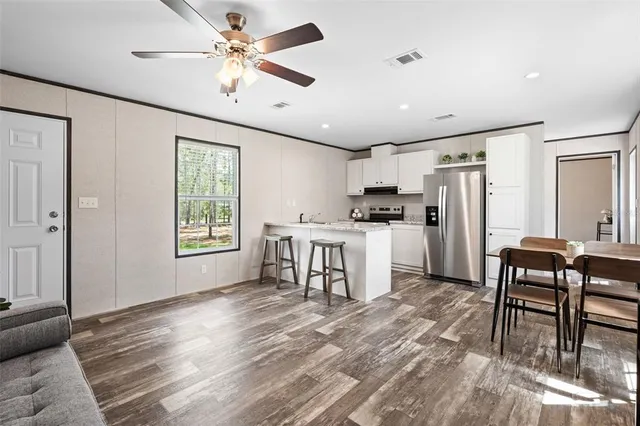 a kitchen with stainless steel appliances kitchen island granite countertop a refrigerator a stove a dining table and chairs with wooden floor