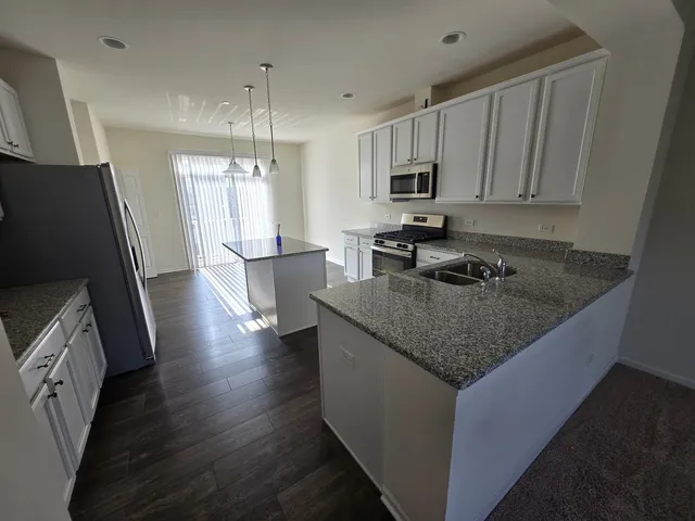 a kitchen with stainless steel appliances granite countertop a refrigerator a sink dishwasher a stove and a dining table with wooden floor