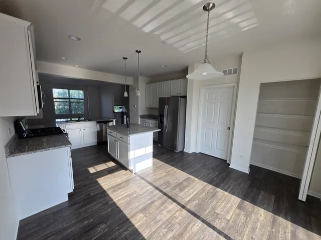 a large white kitchen with a refrigerator a stove a sink and a dining table with wooden floor