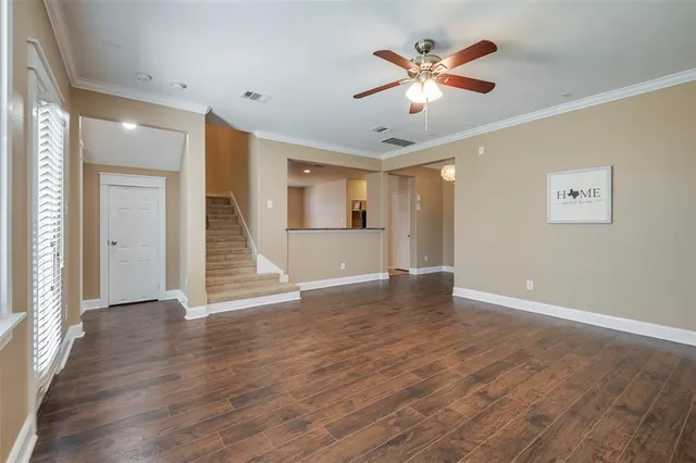 a view of an empty room with wooden floor and a ceiling fan