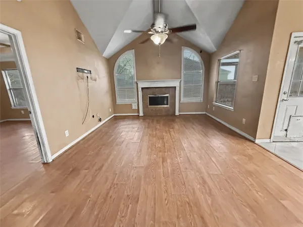 an empty room with wooden floor fireplace and windows
