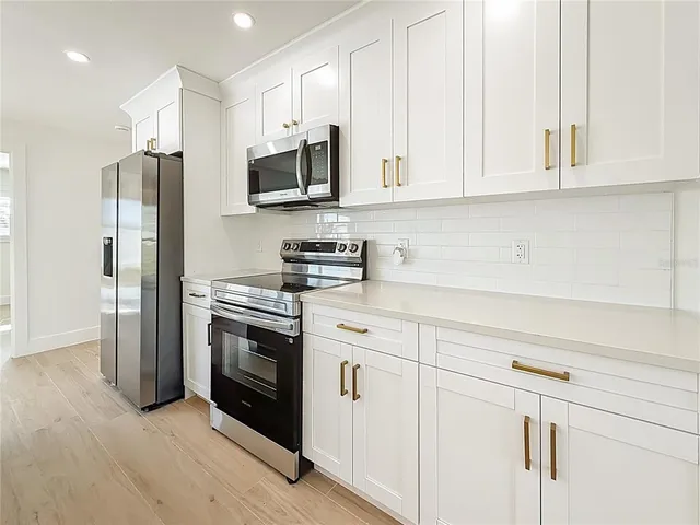 a kitchen with stainless steel appliances granite countertop white cabinets a sink a stove a refrigerator and white cabinets