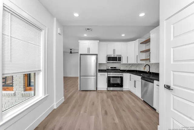 a kitchen with granite countertop white cabinets a stove a sink and dishwasher with wooden floor