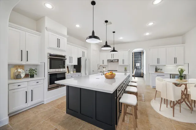 a kitchen with stainless steel appliances kitchen island granite countertop a stove a sink a oven a dining table and chairs with wooden floor