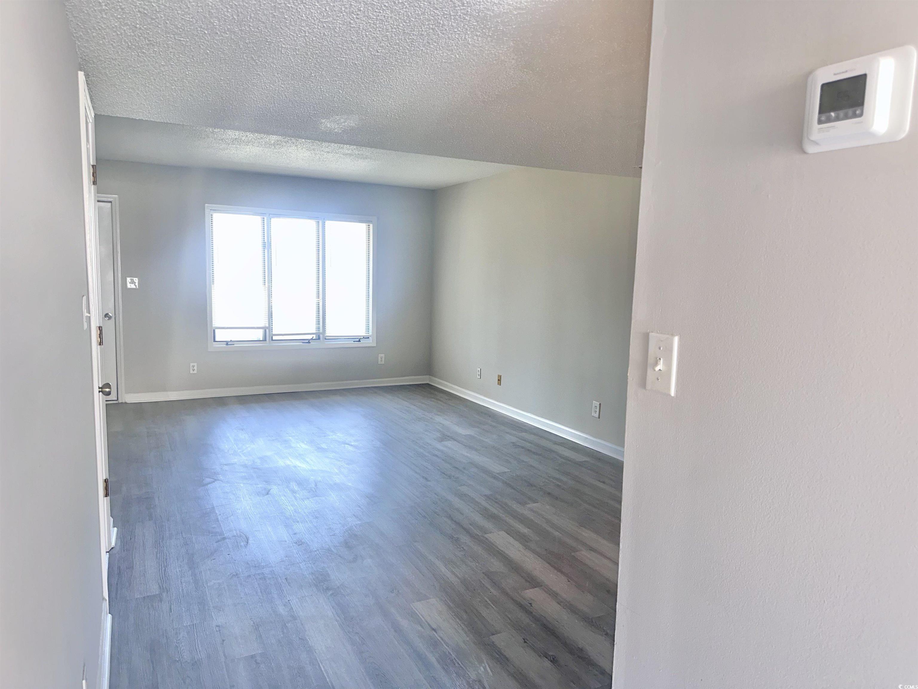401 Garden Drive, Unit 100B Myrtle Beach, SC 29575 - Photo 4 of 23 Spare room featuring dark wood-type flooring and a textured ceiling