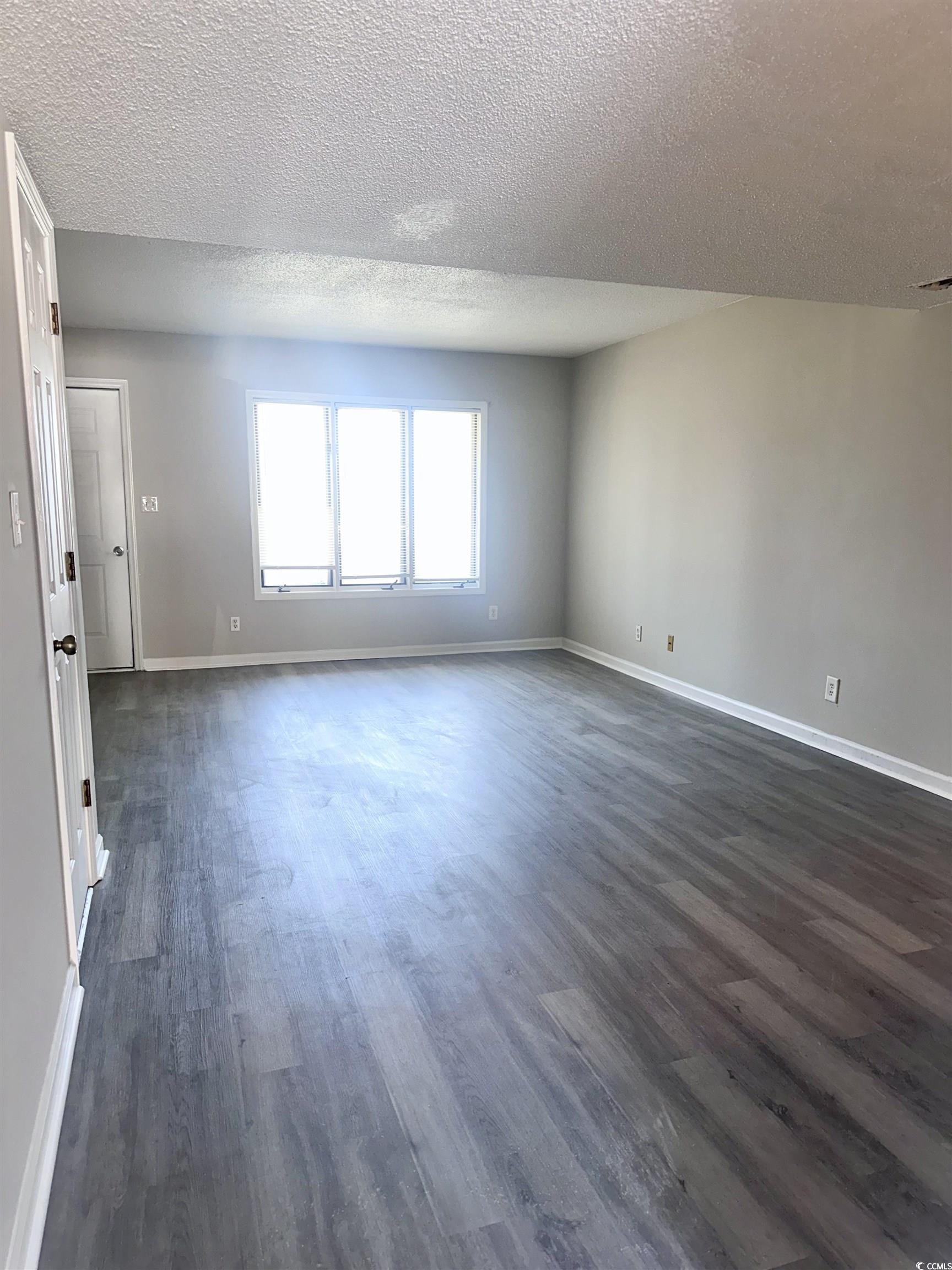 401 Garden Drive, Unit 100B Myrtle Beach, SC 29575 - Photo 6 of 23 Unfurnished room with dark wood-style flooring and a textured ceiling
