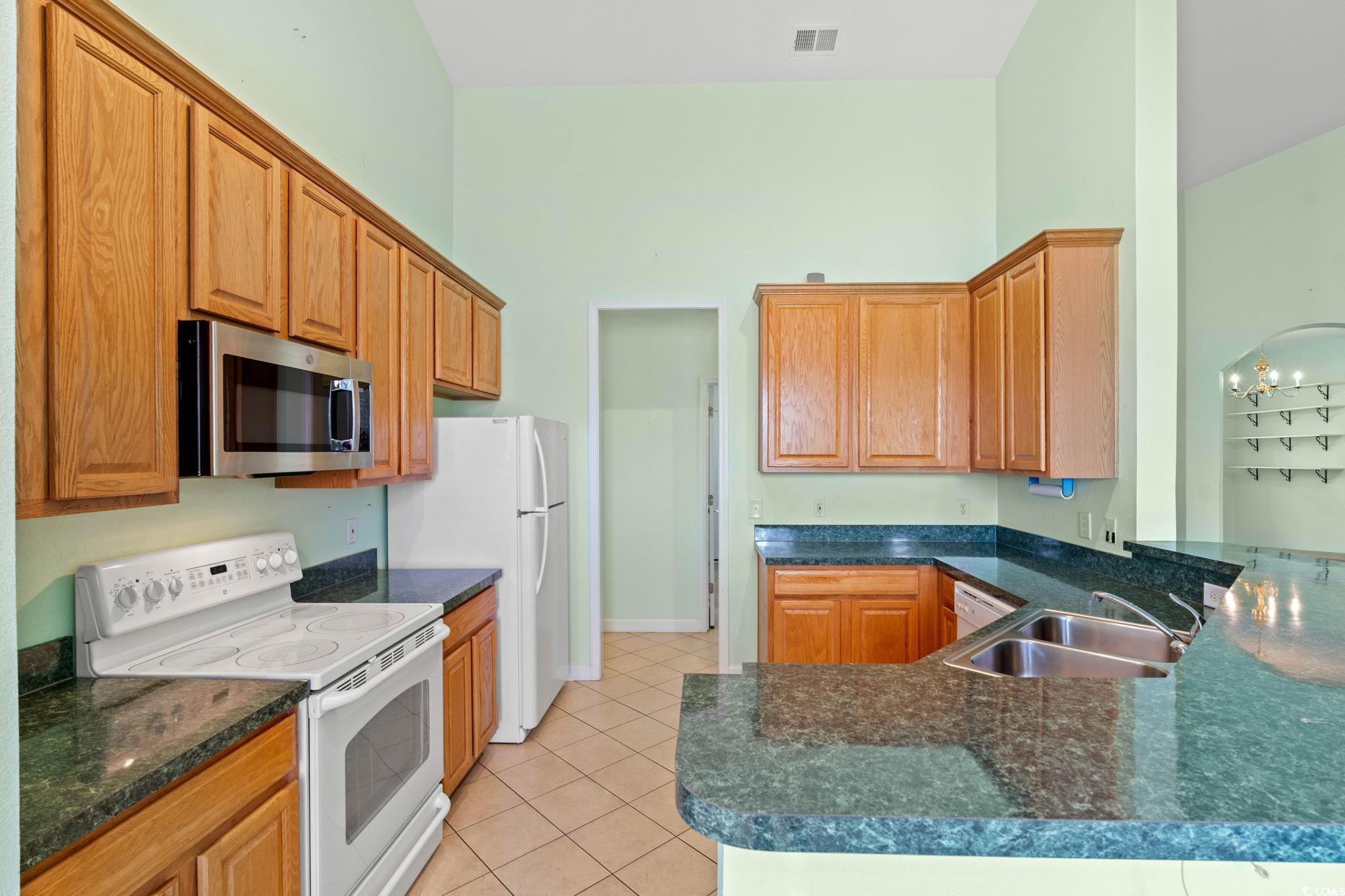 875 Brookline Drive Myrtle Beach, SC 29579 - Photo 11 of 40 Kitchen featuring electric range, light tile patterned floors, stainless steel microwave, brown cabinets, and a peninsula