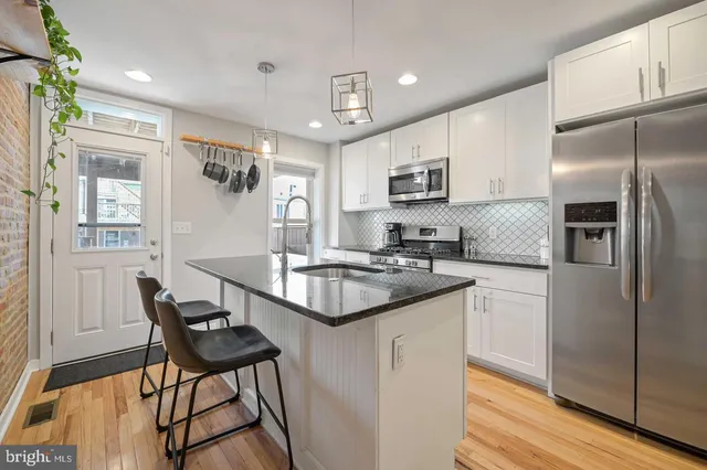 a kitchen with stainless steel appliances granite countertop a stove a sink dishwasher a refrigerator and a dining table with wooden floor