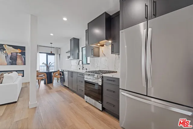 a kitchen with stainless steel appliances granite countertop a refrigerator a sink a stove and a wooden floors