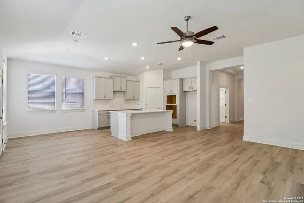 a view of a livingroom with a ceiling fan & kitchen space