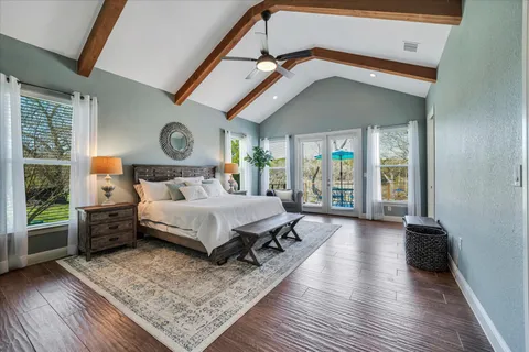 a spacious bedroom with a bed a mirror and a large window with wooden floor