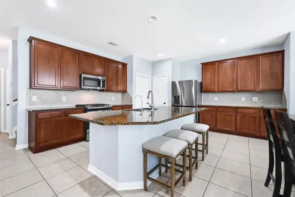 a kitchen with kitchen island granite countertop wooden cabinets a stove a microwave a island with a dining table and chairs