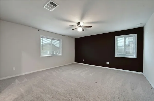 an empty room with ceiling fan and kitchen view