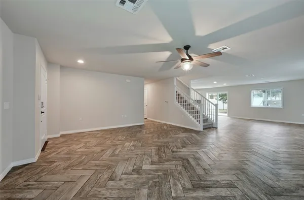 a view of an empty room with wooden floor and a ceiling fan