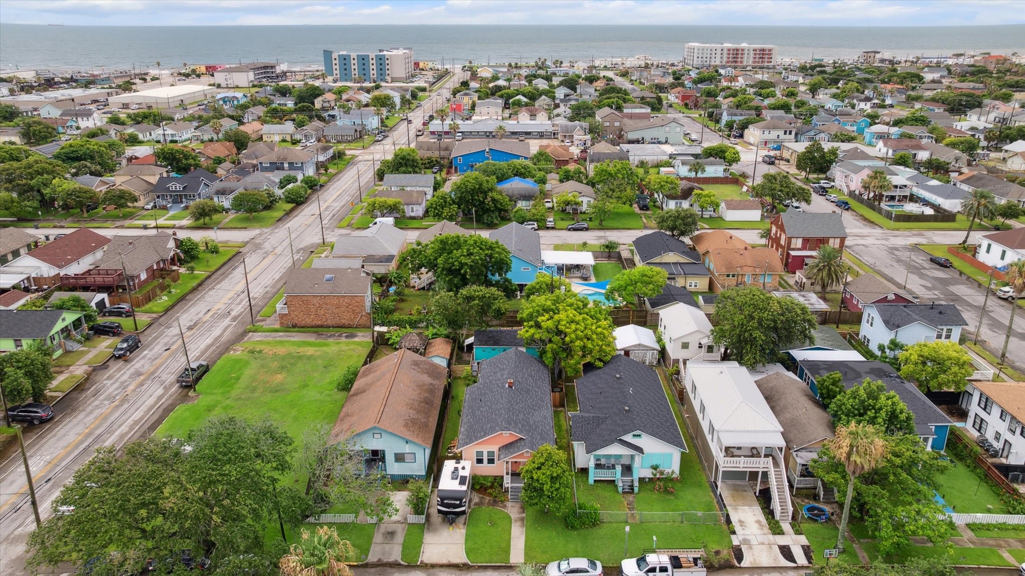 4109 Avenue R Galveston, TX 77550 - Photo 3 of 18 This aerial photo showcases a charming neighborhood with a mix of colorful, well-maintained homes. The area is lush with greenery and has a coastal vibe, as the ocean is visible in the background. The streets are quiet and residential, offering a peaceful setting.
