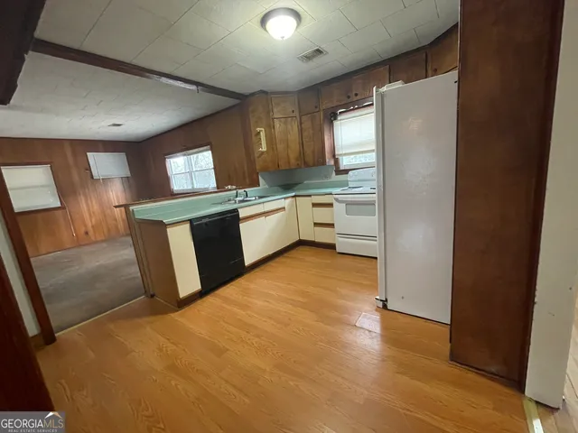 a large kitchen with a refrigerator a sink dishwasher a stove and white cabinets with wooden floor