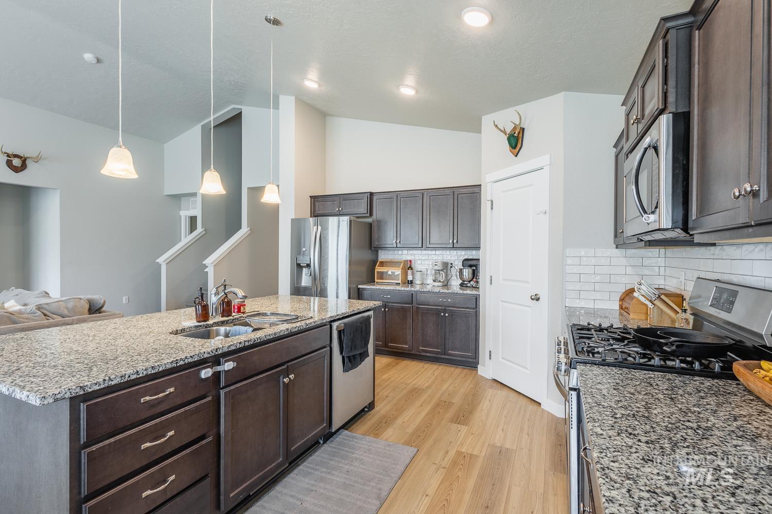 12623 Shadow Peak Street Caldwell, ID 83607 - Photo 16 of 50 Kitchen featuring granite countertops, wood-finish flooring, dark wood cabinetry, a subway tile backsplash, and stainless steel appliances