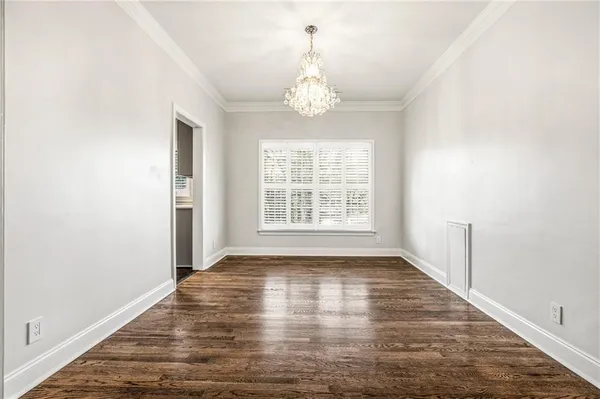 an empty room with wooden floor chandelier and windows
