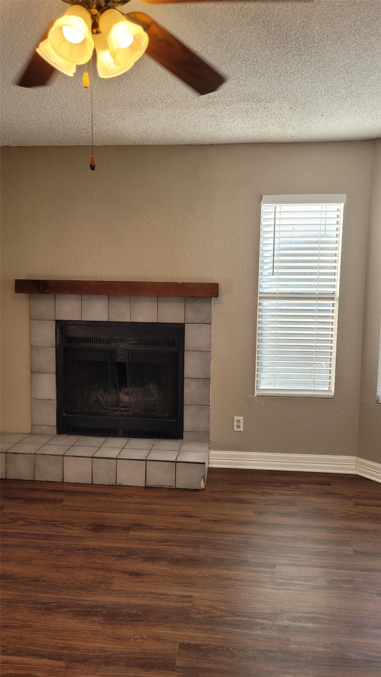 Detailed view of a textured ceiling, a tile fireplace, wood finished floors, and a ceiling fan