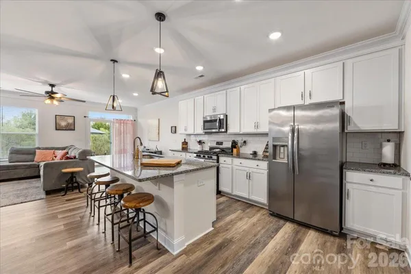 a kitchen with stainless steel appliances granite countertop a refrigerator a stove top oven a dining table and chairs with wooden floor