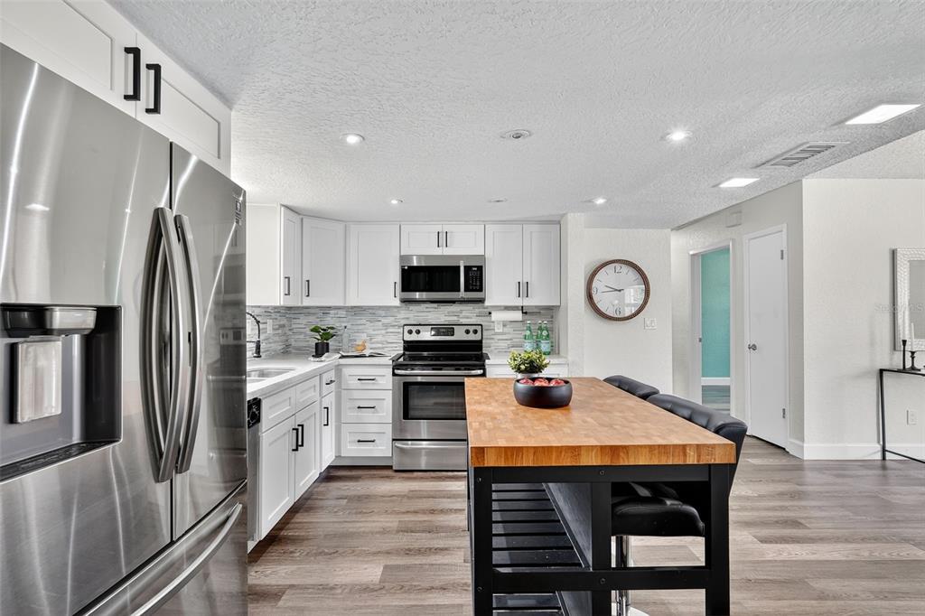 11119 Temple Avenue Seminole, FL 33772 - Photo 8 of 35 a kitchen with stainless steel appliances granite countertop a refrigerator a stove top oven a sink dishwasher and white cabinets with wooden floor