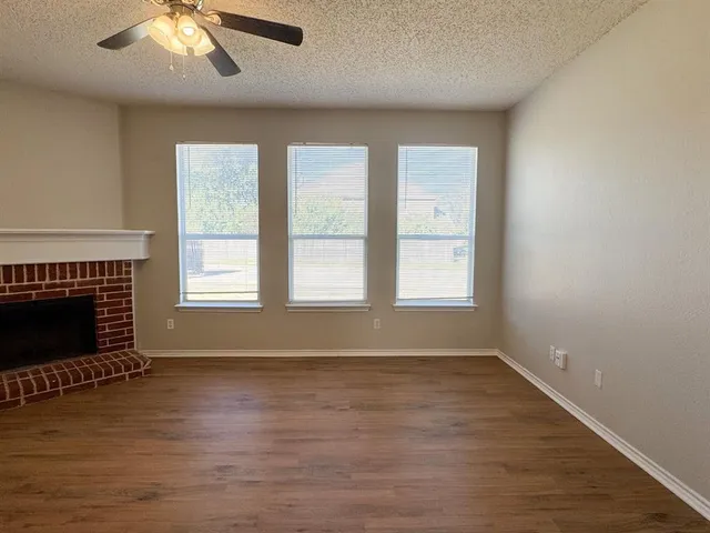 an empty room with wooden floor fireplace and windows